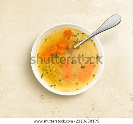 bowl of chicken broth soup on beige color kitchen table, top view