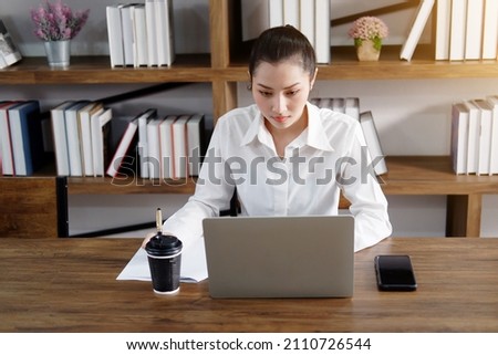 Asian businesswoman is working or online shopping with laptop and drinking hot coffee in workspace at office. Collegian woman are researching information on the Internet in library at the university. Royalty-Free Stock Photo #2110726544