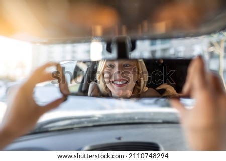 Woman hand adjusting rear view mirror of her car. Happy young woman driver looking adjusting rear view car mirror, making sure line is free visibility is good