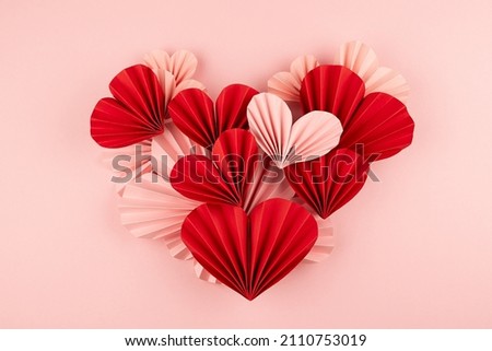 Bright, cute and passion Valentines day background - single heart of mix pink and red paper ribbed hearts in chinese origami style on soft light pastel pink background, top view.