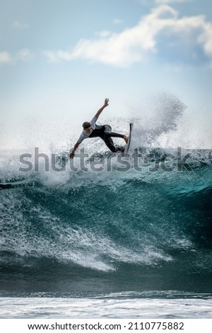 Young surfer with with wetsuit enjoying big waves in Tenerife, Canary Islands. Sporty boy riding his surf board on the ocean wave. Brave teenager making tricks on the rough sea during a competition. Royalty-Free Stock Photo #2110775882