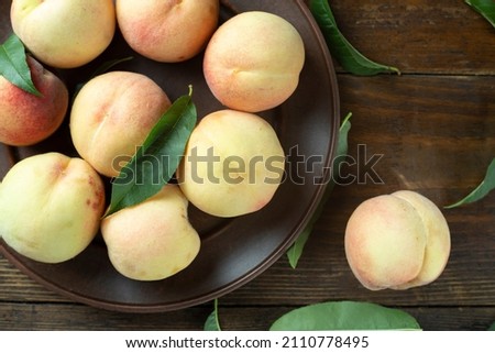 Ripe peaches with leaves in a clay plate on a wooden table. Fresh harvest. Top view.
