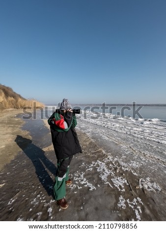 Authentic woman photographer taking pictures of natural frozen lake with a clear blue sky in background. Explorer