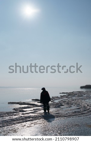 A woman silhouette enjoying winter while walking on a frozen lake with blue sky in the background. Freedom