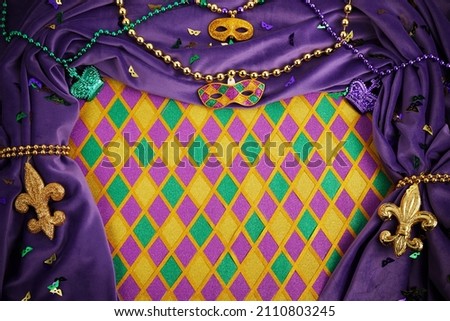 Frame of Mardi Gras Mask and colorful Mardi Gras Beads on diamond shaped background Royalty-Free Stock Photo #2110803245