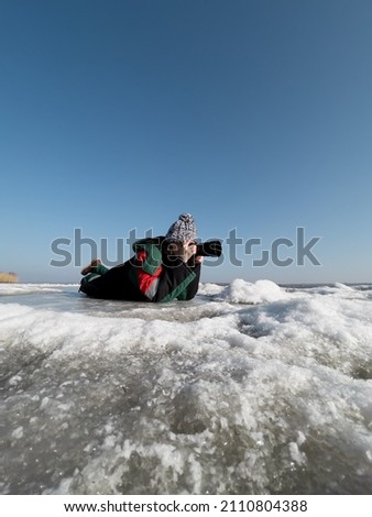 Authentic woman photographer taking pictures of natural frozen lake with a clear blue sky in background. Explorer