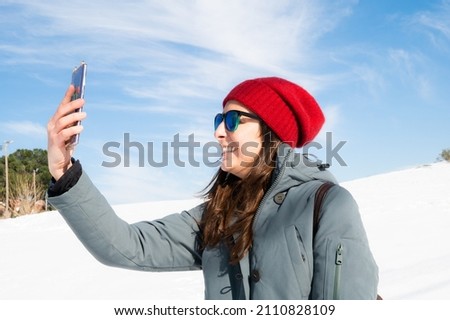 Fashionable girl taking a selfie with her smart phone in a snowy landscape