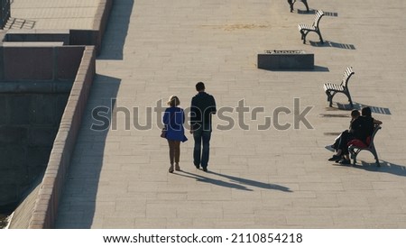 Photography of Moscva river embankment in sunny spring day. The beauty of the capital. One couple of young man and woman sitting on the bench, other walking. View from above, top view