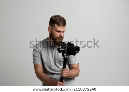 Professional bearded videographer holding camera which set on 3-axis gimbal. Videographer using steadicam. Pro equipment helps to make high quality video without shaking.