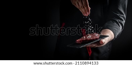 Chef hands cooking meat steak and adding seasoning in a freeze motion. Fresh raw Prime Black Angus beef rump steak. banner, menu recipe. Royalty-Free Stock Photo #2110894133