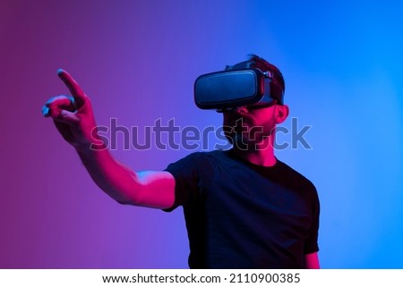 Bearded young man in virtual reality glasses in the studio with blue and pink light.