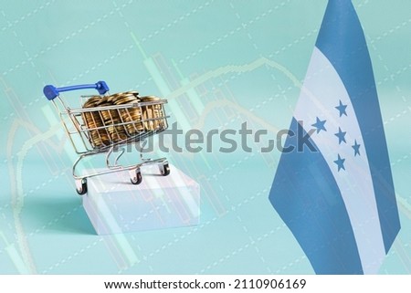 A metal basket filled with coins and the flag of Honduras on a blue podium, a sales chart on the background. The concept of GDP and economic indicators of Honduras