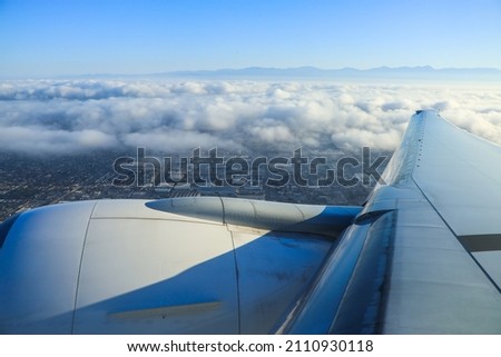Sitting on the airplane, through the window overlooking the ground. Background is sea ​​of ​​clouds, buildings and blue sky. Royalty-Free Stock Photo #2110930118