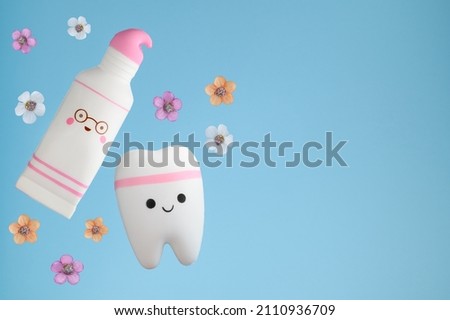 Dental spring summer concept. Stomatology. Toy tooth and toothpaste on a blue background with flowers. Prevention of healthy teeth, care.