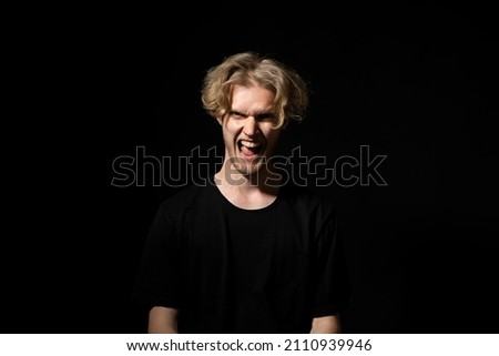Young brutal angry man in black t-shirt screams over black background. Face expression. Crazy man. Negative emotions, problems. Stressed guy shouting.
