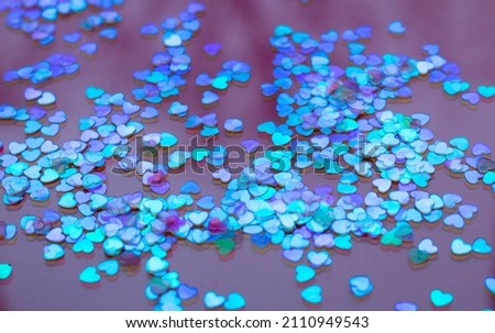Confetti in the form of lilac hearts on a red background. The word love is lined with confetti.