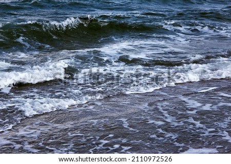 Strong waves with bright white sea foam. The raging sea in bad weather. Dark sea or ocean. An incoming wave close up. Storm waves at sea. Abstract natural background. 