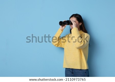 Studio photo with blue background of an asian woman looking through binoculars