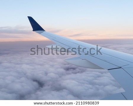 Aerial view of the wing of an airplane flying over the Atlantic Ocean, with a radiant sunrise tinting the fluffy clouds in a beautiful orange color. Concept traveler, vacations, passenger, wing.