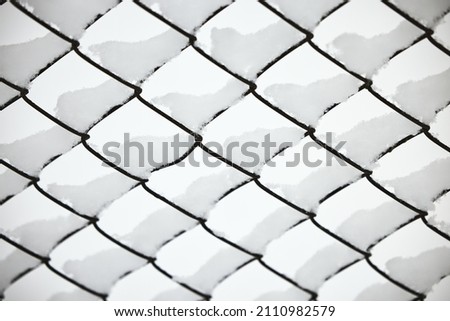 Snow on a mesh fence close-up, snow fence. Abstract winter background. Snow on a wire fence