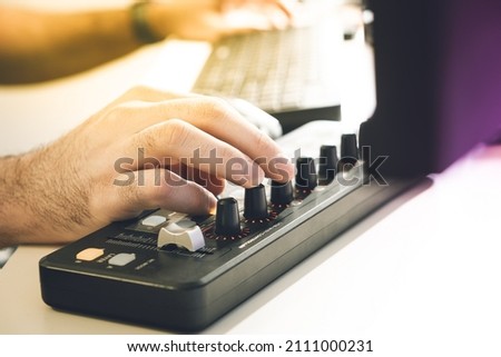 
Man works at a mixing console, a midi controller is connected to a personal computer, a man's hand on the keys