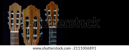Spanish guitars for an instrumental concert concept. Perfect musical instruments on a black background. Guitar heads, necks, and silver and nylon strings. Ensemble performance, party. Royalty-Free Stock Photo #2111006891