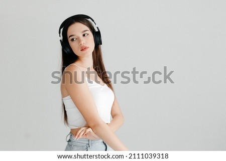 Young woman wearing casual clothes - white top and jeans, black headphones, listening to