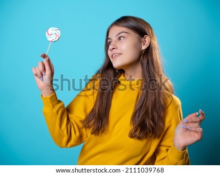 Beautiful young brunette with a lollipop in her hands, sweet candy, portrait in yellow on a blue background, bright colors