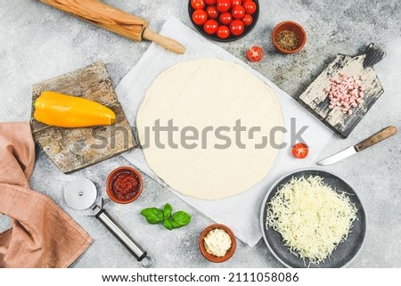 Pizza ingredients: cherry tomato, pepper, cheese, ham, basil with dough rolled out in a circle and a wooden chip lie on the table with copy space, top view close-up. Concept of cooking pizza.