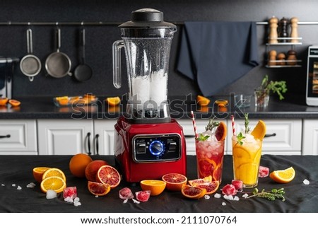 Modern electronic Red blender with crushed ice cubes and cold homemade citrus lemonade in faceted glasses with cardboard cocktail tubes. home kitchen background. Royalty-Free Stock Photo #2111070764