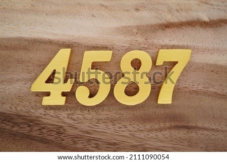 Wooden Arabic numerals 4587 painted in gold on a dark brown and white patterned plank background.