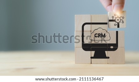 AI-CRM solution concept. Data driven marketing strategy with AI. For marketing plan, providing automated interaction to customer. Hand hold wooden cubes with AI-CRM icon on grey background, copy space Royalty-Free Stock Photo #2111136467