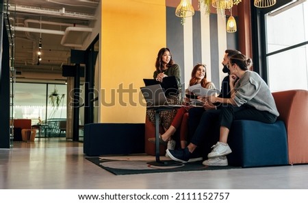 Diverse businesspeople working in an office lobby. Group of happy businesspeople having a discussion while sitting together in a co-working space. Young entrepreneurs collaborating on a new project. Royalty-Free Stock Photo #2111152757