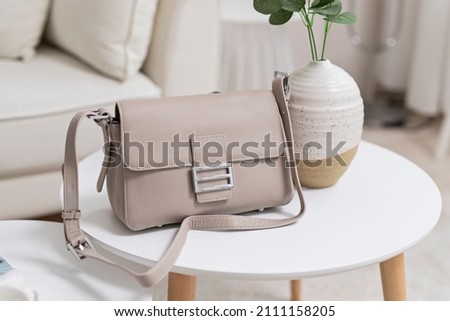 Grey women's leather bag on a white table against the background of a sofa. Royalty-Free Stock Photo #2111158205