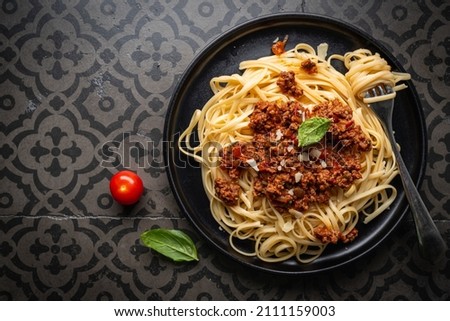 Pasta spaghetti bolognese with minced beef sauce, tomatoes, parmesan cheese and fresh basil in a plate on black tile background. Italian food, top view Royalty-Free Stock Photo #2111159003