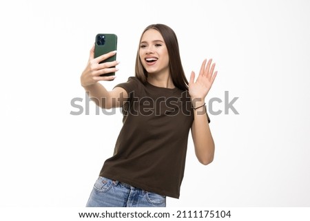 Happy young woman blogger influencer holding modern smart phone wave hand hello. Smiling vlogger girl looking at mobile make video call, shooting vlog taking selfie on grey background