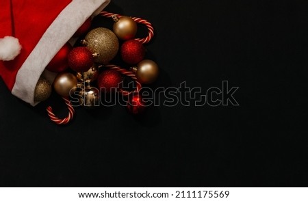 Banner. Christmas hat of Santa Claus, with Christmas caramel candies, toys and sequins on a black background. Copy space. Flatlay