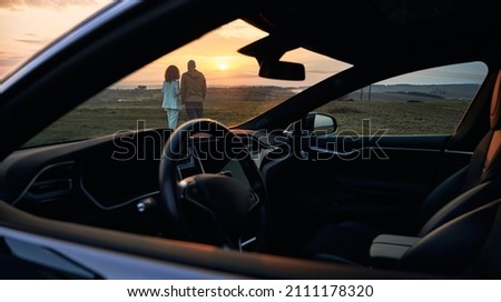 Back view of young couple in love enjoying sunset automobile date at nature environment, husband and wife spending evening for bonding togetherness with black car for trip travelling on front Royalty-Free Stock Photo #2111178320
