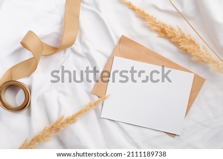 Styled craft envelope and white card mockup with dried grass on textile