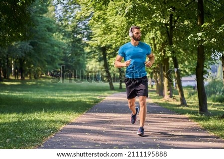 Young man running in park with headphones on sunny summer day Royalty-Free Stock Photo #2111195888