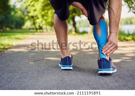 Runner holding injured achilles tendon with kinesiology tape Royalty-Free Stock Photo #2111195891