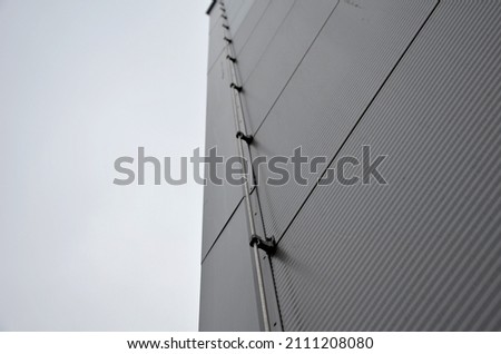 The lightning conductor is used to protect buildings from lightning, which can damage the house or industrial hall. grounding wire routing along a gray metal sheet facade. plastic holders