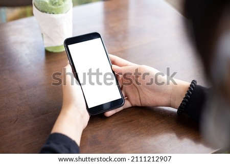 Woman hand using smartphone In the coffee shop Screen blank with clipping path ,Top view mockup image of girl holding mobile phone with empty white screen