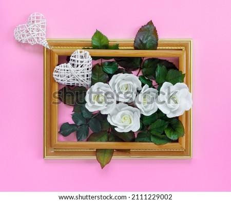 Beautiful white roses with green foliage and hearts in vintage wooden frame on bright pink wall for Valentine's Day. Creative greeting card.
Copy space for your text.
