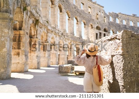 woman in hat stands and looking on Coliseum in Pula Croatia. travel concept.Young woman enjoy summer Italian vacation in Europe. Royalty-Free Stock Photo #2111251301