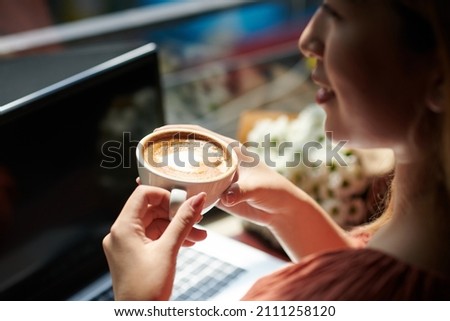 Woman drinking morning coffee and working working on computer in coffeeshop Royalty-Free Stock Photo #2111258120