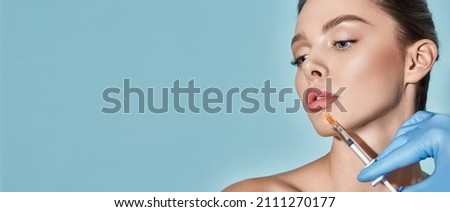 Lips filler injection for beautiful woman's lip augmentation with beautician on blue background. Lip augmentation procedure Royalty-Free Stock Photo #2111270177