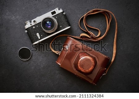 Old shabby retro camera and leather carrying case on black graphite background in close-up, flat lay
