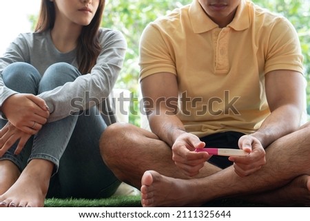 Unhappy Asian woman holding and looking pregnancy test and a negative result her worried about the relationship with her husband Problems arising from infertility. Concept of infertility and medical Royalty-Free Stock Photo #2111325644