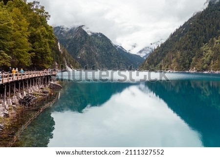 Horizontal view of the people walking along the plank road on the shores of the Long Lake in Jiuzhaigou Valley Scenic Area, Sichuan, China. UNESCO World Heritage site in China  Royalty-Free Stock Photo #2111327552